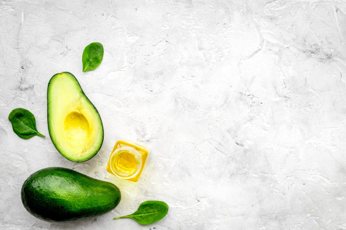 Natural products for skin care. Avocado oil in bottles near sliced avocado on grey background top view.