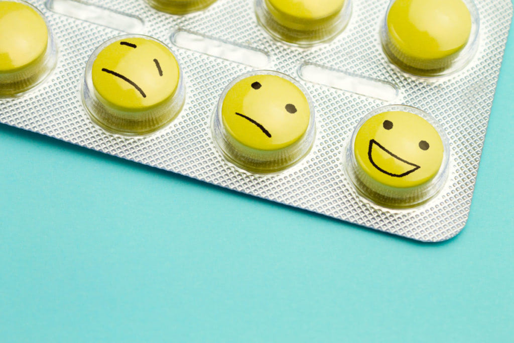 Yellow pills andfunny faces in a blister on a blue background. The concept of antidepressants and healing