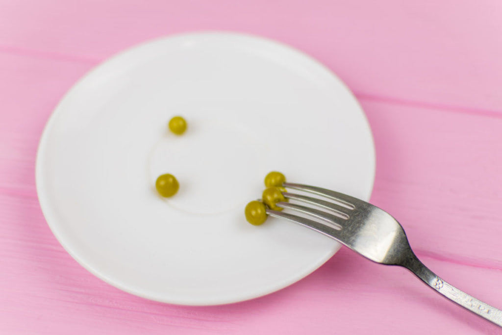 The concept of starvation, bulimia. A pea on a fork on a white plate.