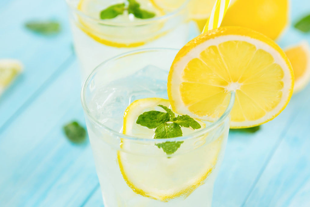 Refreshing drinks for summer, cold sweet and sour lemonade juice with ice cubes in the glasses garnished with sliced fresh lemons