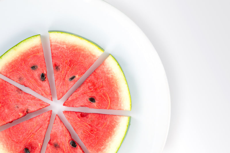 Watermelon slices arranged on a white plate on a white background with copy space