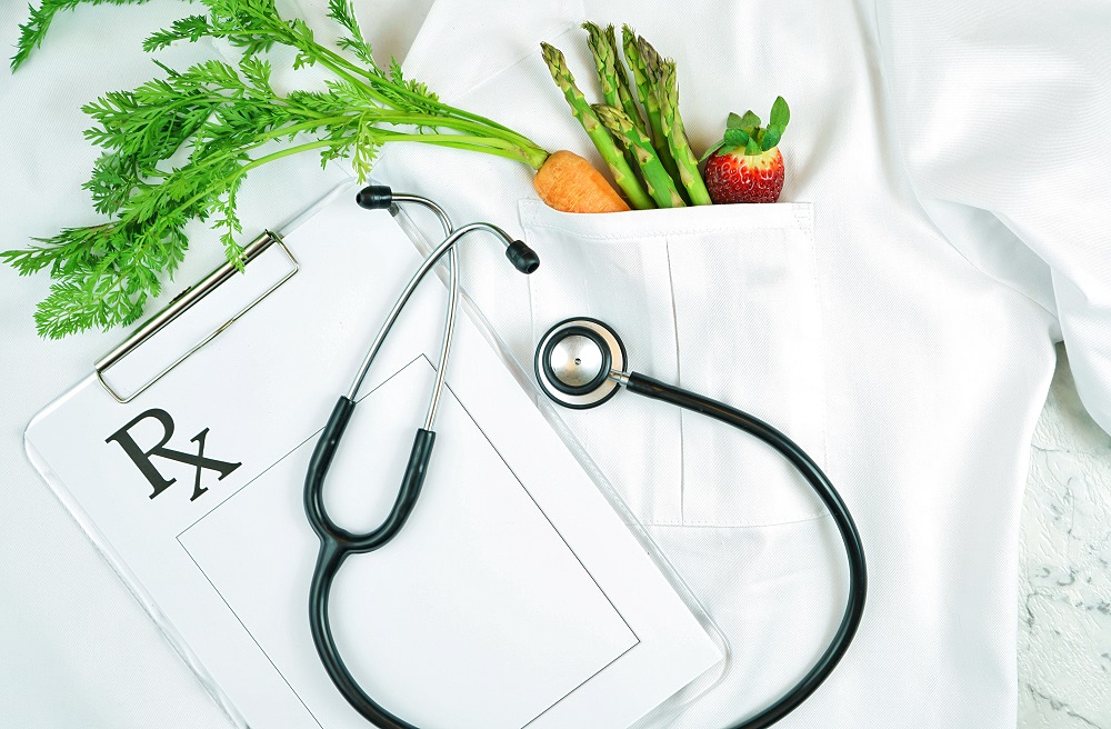 Healthy lifestyle, food is medicine, concept flatlay with fruit and vegetables in pocket of white doctor's coat with clipboard and stethoscope.