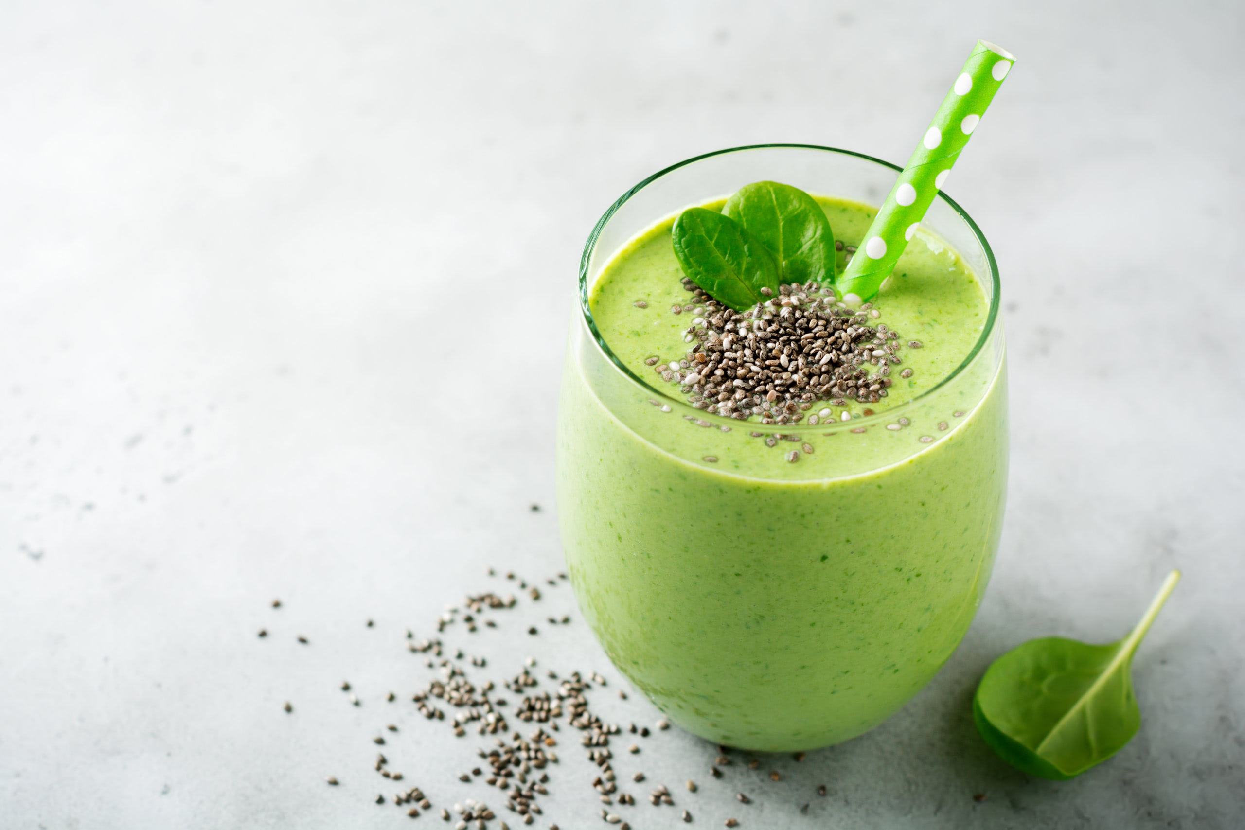 Vegetarian healthy green smoothie from avocado, spinach leaves, apple and chia seeds on gray concrete background. Selective focus. Space for text.