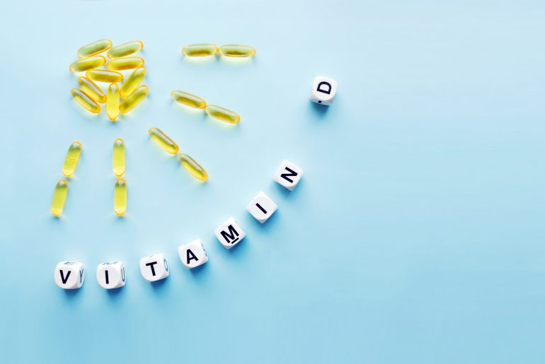 Yellow capsules in the form of the sun with rays and the word vitamin D from white cubes with letters on a blue background. VITAMIN D word for healthy and medical concept. Sunshine vitamin